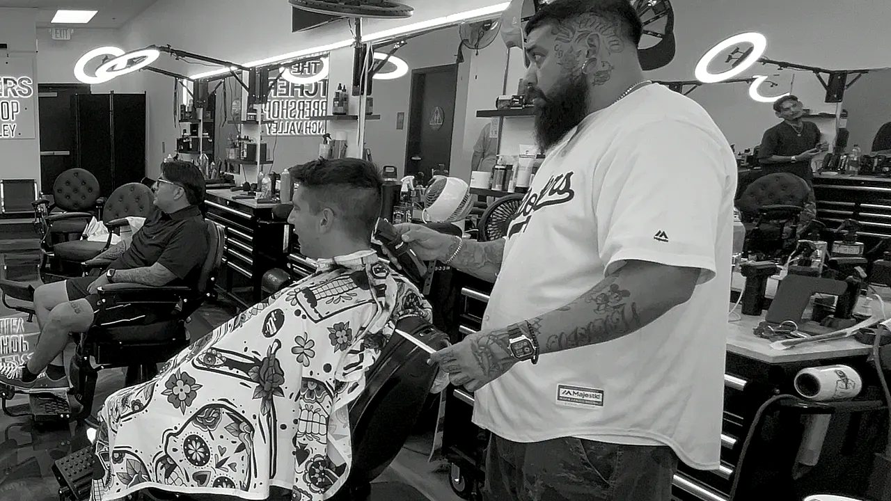 Barber working a fade with clippers on a client in the tattoo-print cape, French Valley floor