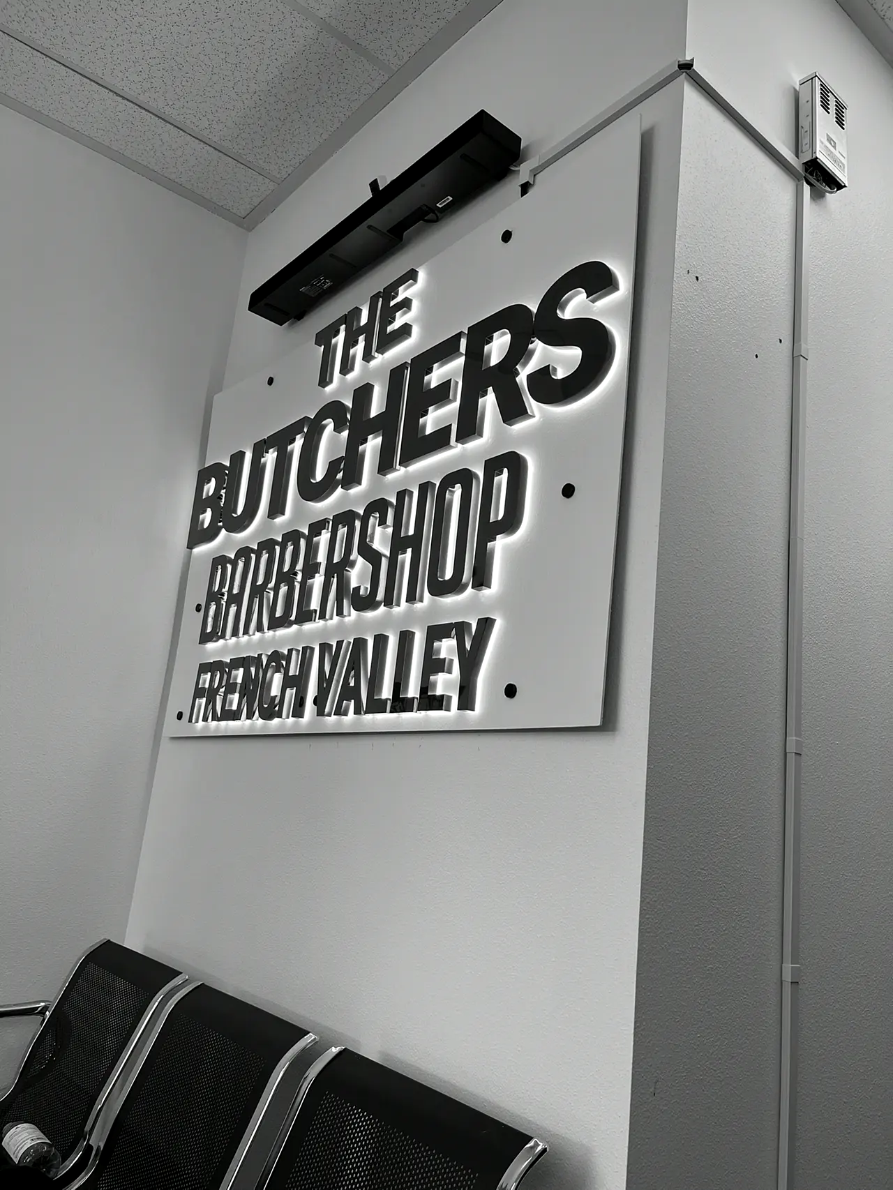 The Butchers Barbershop French Valley sign — black dimensional letters on a white wall under a linear LED light