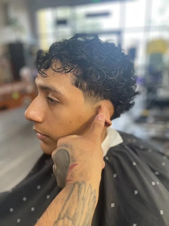 Curly top fade — defined curls up top with the sides faded and lined up, barber checking the edge by the ear